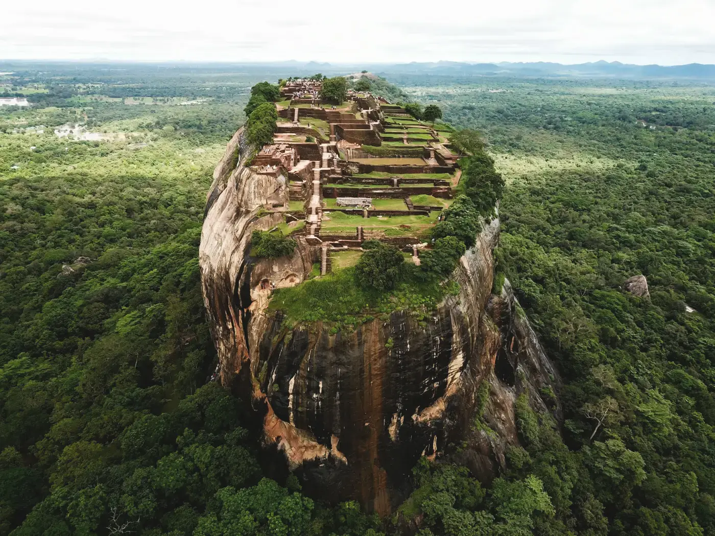 Aerial view of Sigiriya, a ruined fortress on a rock plateau standing far above flat jungle in every direction. The vantage this post is about: you cannot see the shape of the terrain you are standing in until you get outside it.