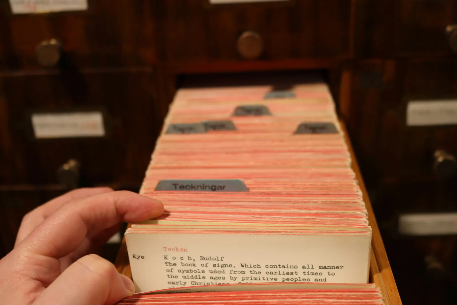 A hand flipping through an open library card catalog drawer: a curated index that takes you straight to the right card instead of every card.